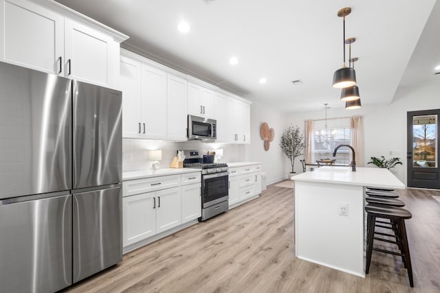 kitchen with pendant lighting, sink, stainless steel appliances, an island with sink, and white cabinets