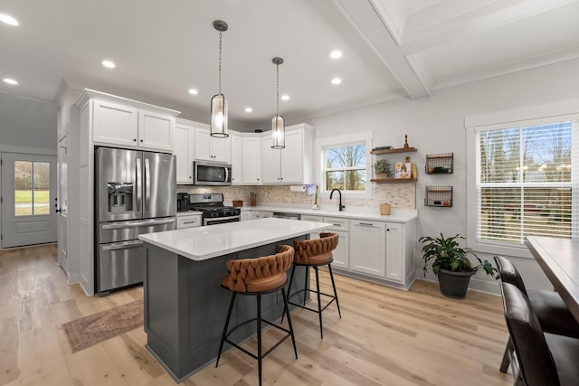 kitchen featuring stainless steel appliances, white cabinetry, a kitchen island, and pendant lighting