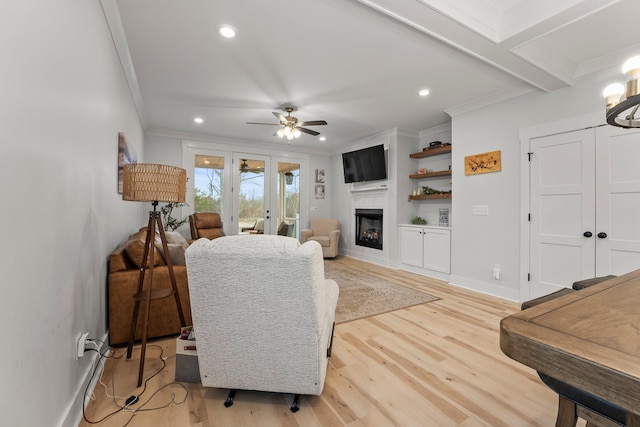 living room featuring french doors, crown molding, light hardwood / wood-style flooring, a large fireplace, and ceiling fan