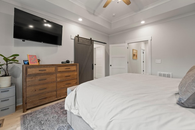 bedroom featuring ornamental molding, a tray ceiling, ceiling fan, a barn door, and light hardwood / wood-style floors