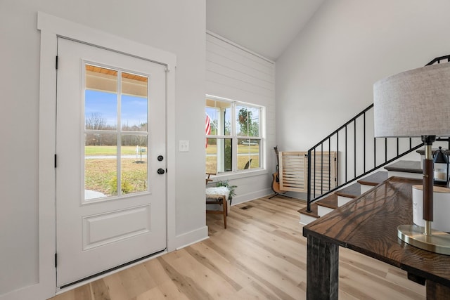 doorway to outside with high vaulted ceiling and light hardwood / wood-style flooring