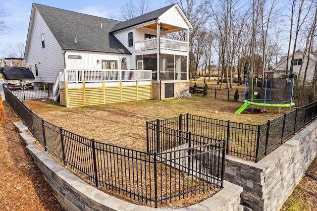 rear view of house with ceiling fan, a trampoline, a yard, a sunroom, and a balcony