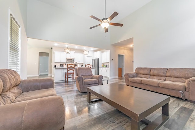 living room with ceiling fan with notable chandelier, hardwood / wood-style floors, and a high ceiling