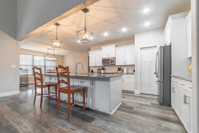 kitchen with stone countertops, pendant lighting, white cabinetry, stainless steel appliances, and a center island with sink