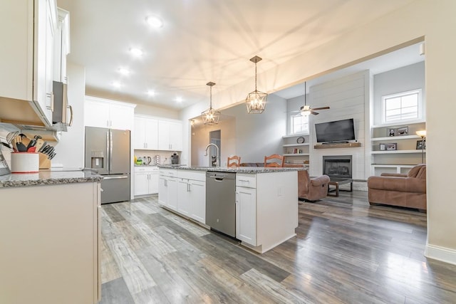 kitchen with pendant lighting, appliances with stainless steel finishes, white cabinetry, a kitchen island with sink, and light stone counters