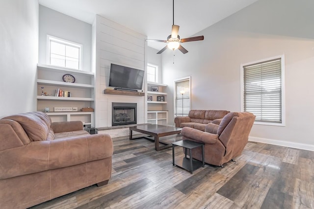 living room featuring a fireplace, dark wood-type flooring, ceiling fan, and a high ceiling