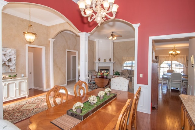 dining space with dark wood-type flooring, ornamental molding, decorative columns, and ceiling fan with notable chandelier