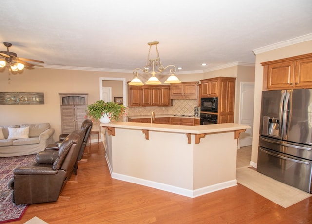 kitchen featuring a breakfast bar area, light hardwood / wood-style flooring, hanging light fixtures, decorative backsplash, and black appliances