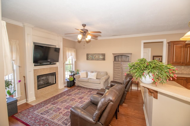 living room with a tile fireplace, ornamental molding, ceiling fan, and light wood-type flooring