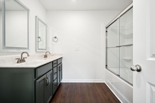 full bathroom with double vanity, baseboards, wood finished floors, combined bath / shower with glass door, and a sink