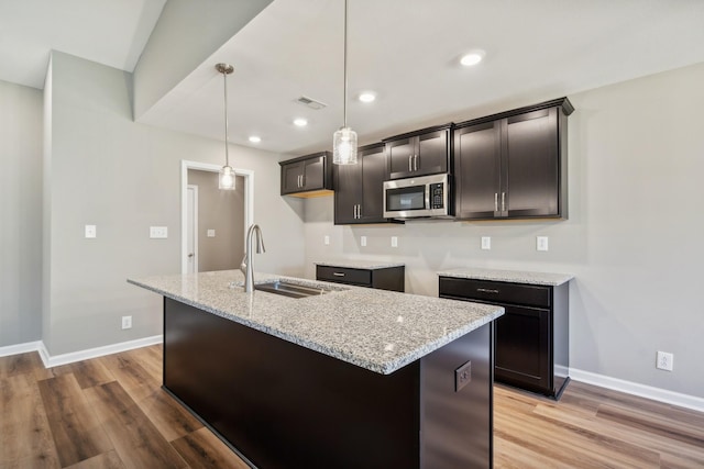 kitchen with light stone countertops, sink, a center island with sink, and decorative light fixtures