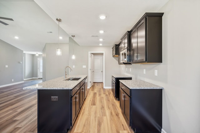 kitchen with sink, pendant lighting, a kitchen island with sink, and light wood-type flooring