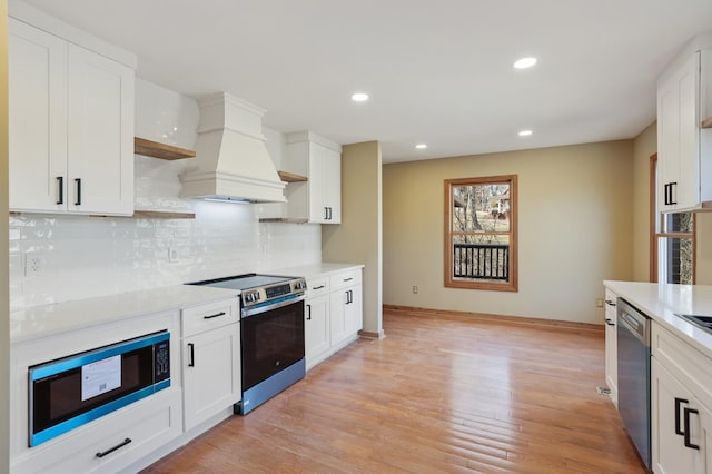 kitchen featuring premium range hood, appliances with stainless steel finishes, white cabinets, decorative backsplash, and light wood-type flooring