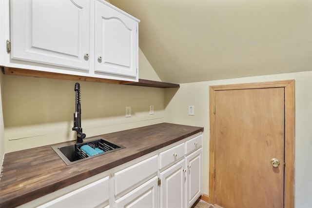 kitchen featuring wood counters, lofted ceiling, sink, and white cabinets