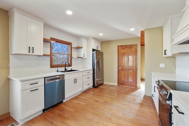 kitchen featuring premium range hood, appliances with stainless steel finishes, sink, white cabinets, and light hardwood / wood-style flooring