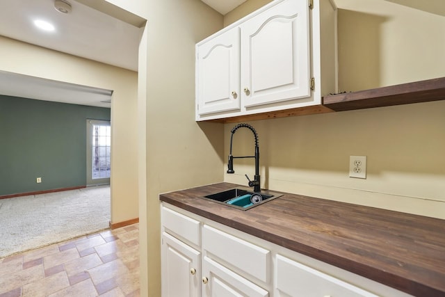 kitchen with white cabinetry, sink, light carpet, and wooden counters