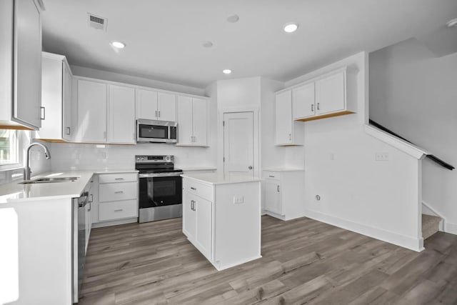 kitchen featuring appliances with stainless steel finishes, white cabinetry, sink, a center island, and light hardwood / wood-style flooring