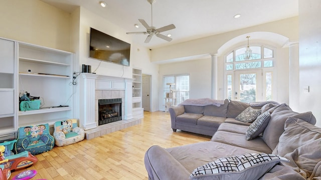 living room with light hardwood / wood-style flooring, a towering ceiling, ceiling fan, a fireplace, and decorative columns