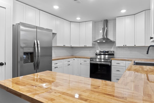 kitchen with stainless steel appliances, white cabinets, wood counters, and wall chimney exhaust hood