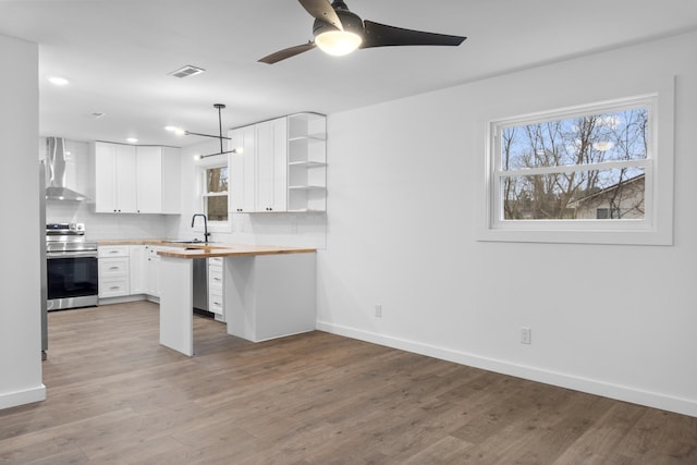 kitchen featuring electric stove, wall chimney range hood, butcher block counters, white cabinets, and decorative light fixtures