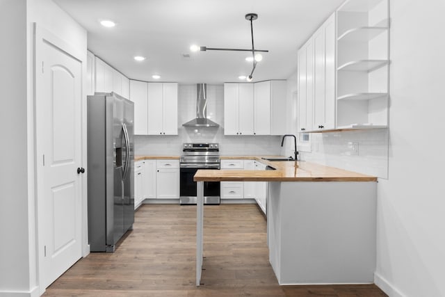 kitchen with wood counters, wall chimney exhaust hood, white cabinetry, decorative light fixtures, and stainless steel appliances