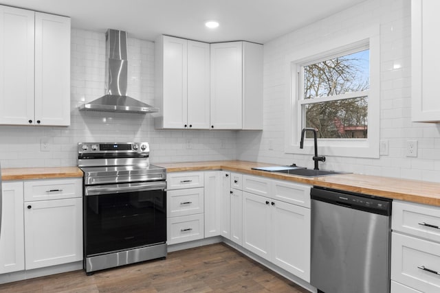 kitchen featuring wood counters, wall chimney range hood, white cabinetry, and appliances with stainless steel finishes