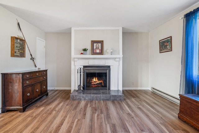 living room featuring light wood-type flooring, a fireplace, and baseboard heating