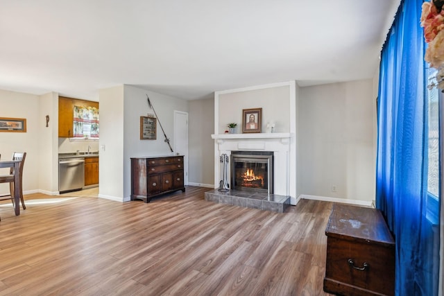 unfurnished living room with a tile fireplace, sink, and light wood-type flooring