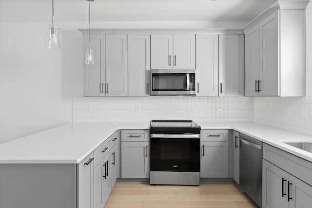 kitchen featuring gray cabinetry, decorative light fixtures, light wood-type flooring, and appliances with stainless steel finishes