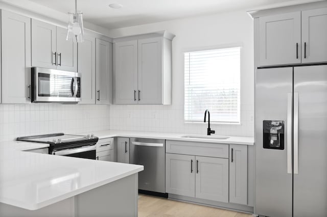 kitchen with sink, tasteful backsplash, gray cabinets, pendant lighting, and stainless steel appliances