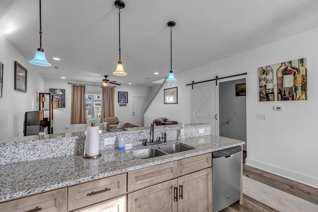 kitchen featuring light brown cabinetry, sink, stainless steel dishwasher, and a barn door