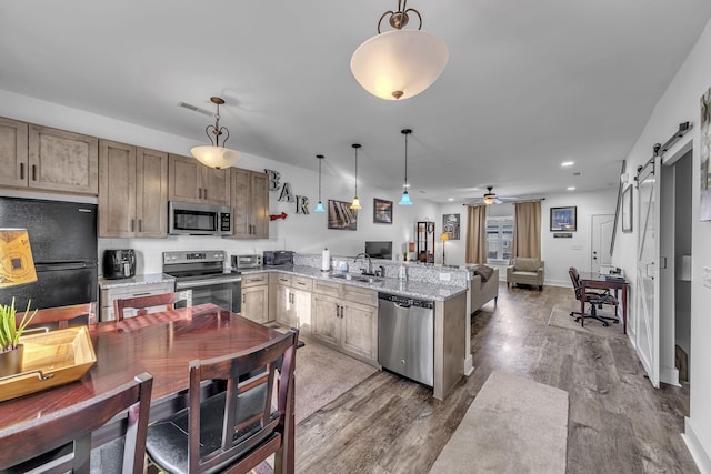 kitchen with decorative light fixtures, kitchen peninsula, stainless steel appliances, a barn door, and light stone countertops