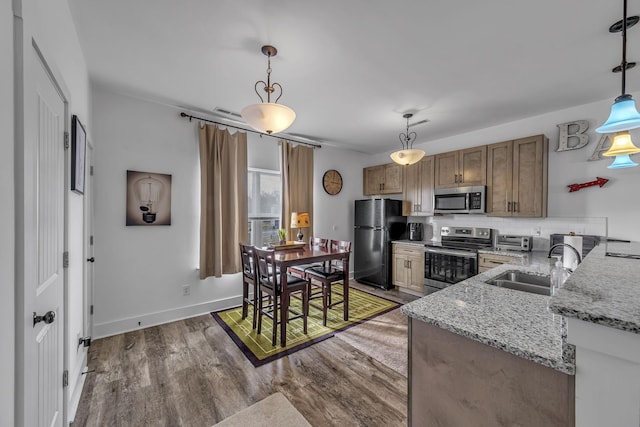 kitchen featuring sink, dark wood-type flooring, appliances with stainless steel finishes, light stone counters, and decorative light fixtures