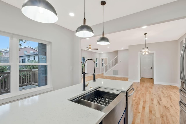 kitchen featuring sink, light hardwood / wood-style flooring, dishwasher, hanging light fixtures, and light stone countertops