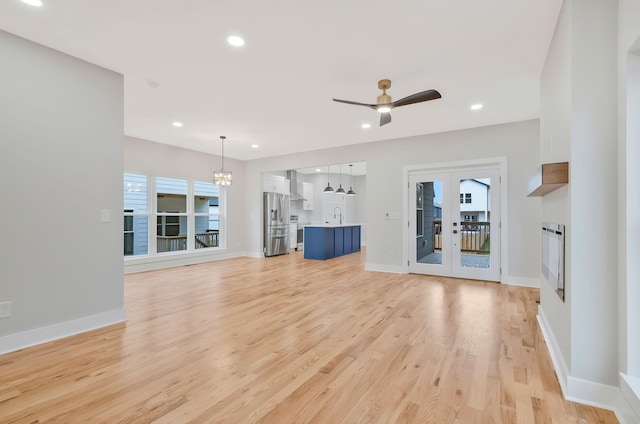 unfurnished living room with sink, ceiling fan with notable chandelier, light wood-type flooring, and french doors