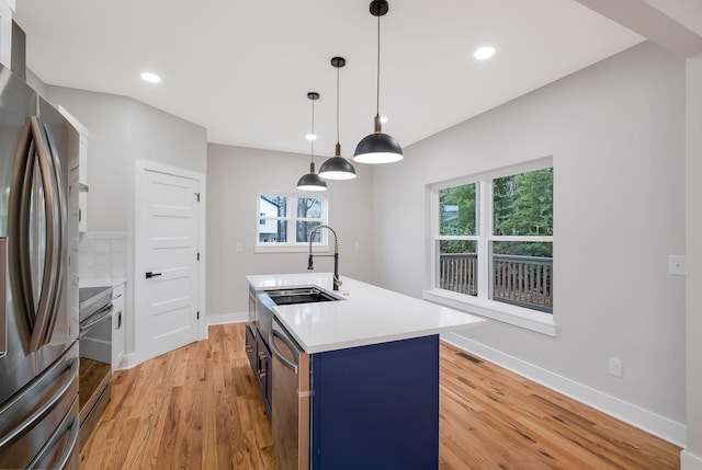 kitchen with pendant lighting, sink, light hardwood / wood-style flooring, stainless steel appliances, and an island with sink