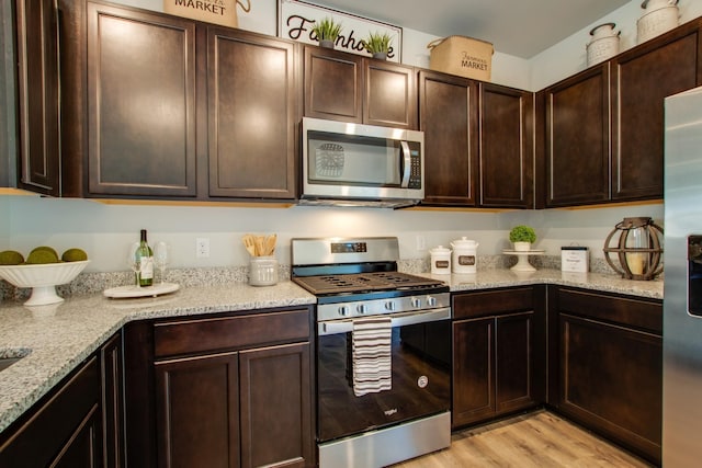 kitchen featuring stainless steel appliances, light wood-type flooring, light stone counters, and dark brown cabinetry