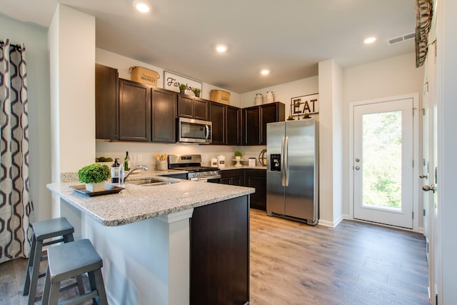 kitchen featuring dark brown cabinetry, appliances with stainless steel finishes, a kitchen breakfast bar, kitchen peninsula, and light hardwood / wood-style floors