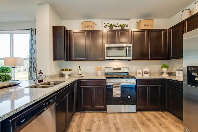 kitchen with sink, light hardwood / wood-style flooring, appliances with stainless steel finishes, dark brown cabinetry, and light stone countertops