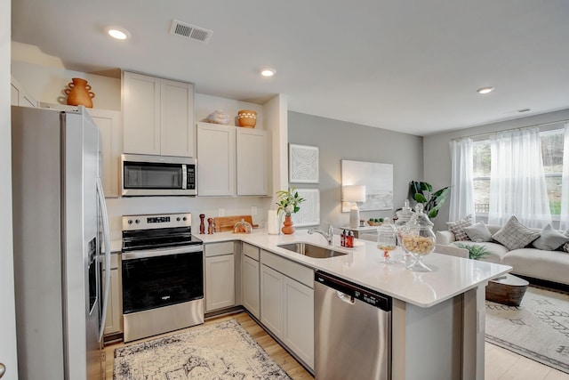 kitchen with appliances with stainless steel finishes, sink, light wood-type flooring, and kitchen peninsula