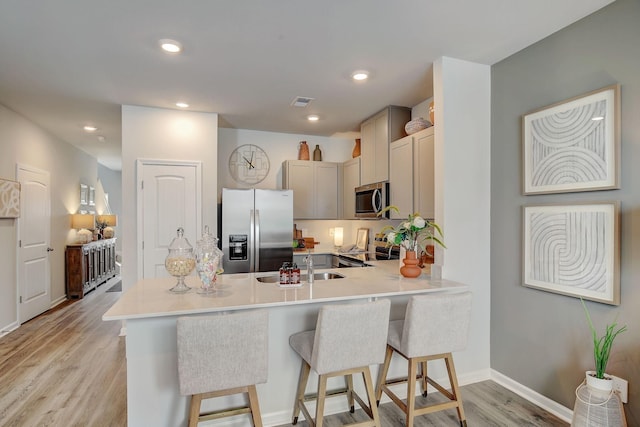 kitchen with sink, light hardwood / wood-style flooring, appliances with stainless steel finishes, a kitchen breakfast bar, and kitchen peninsula