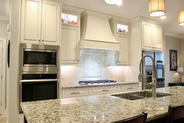 kitchen featuring sink, custom exhaust hood, ornamental molding, light stone counters, and stainless steel appliances