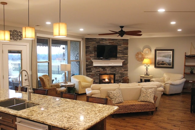 living room featuring sink, crown molding, ceiling fan, dark hardwood / wood-style flooring, and a stone fireplace