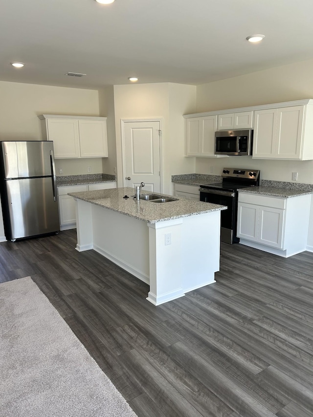 kitchen featuring light stone counters, a sink, appliances with stainless steel finishes, white cabinets, and dark wood-style flooring