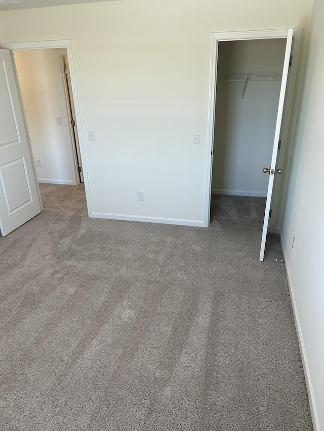 unfurnished bedroom featuring baseboards, a closet, carpet floors, and a spacious closet