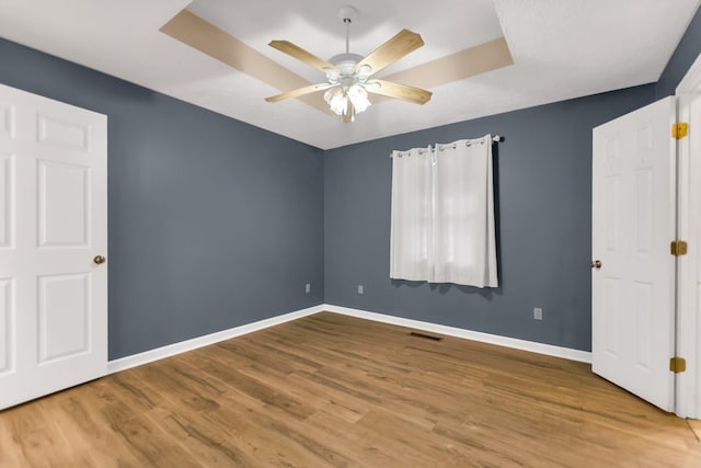 unfurnished bedroom featuring ceiling fan, wood-type flooring, and a raised ceiling