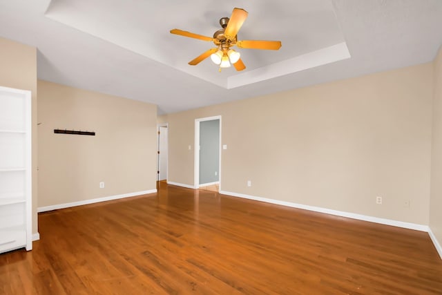 unfurnished room with ceiling fan, a tray ceiling, and dark hardwood / wood-style flooring