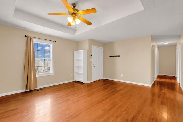 unfurnished room with hardwood / wood-style flooring, a raised ceiling, and ceiling fan