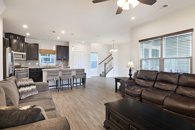 living room featuring ceiling fan with notable chandelier and light wood-type flooring