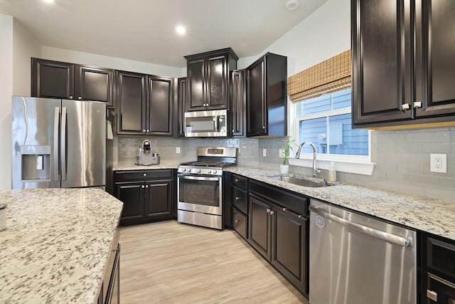 kitchen with stainless steel appliances, a sink, light wood finished floors, and light stone counters